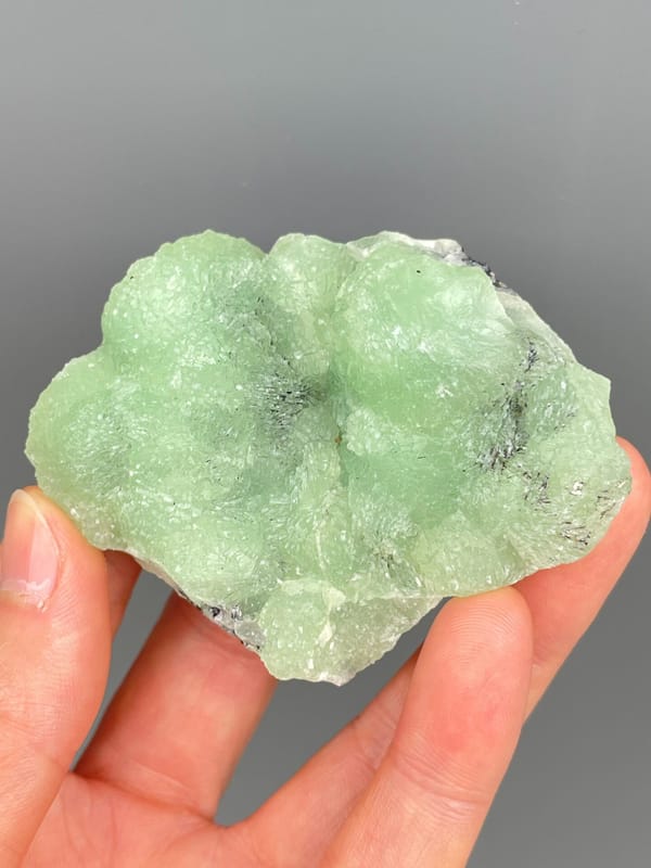 Apple-green botryoidal prehnite plate from Sichuan, China, held in hand