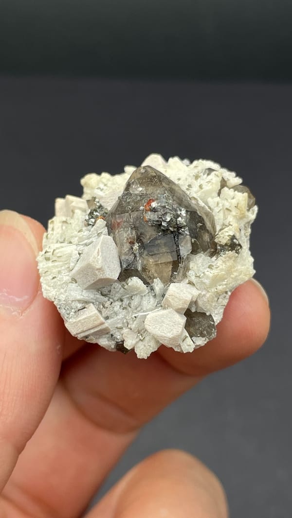 Smoky quartz crystal in cream feldspar from Yunxiao, Fujian, China, held in hand