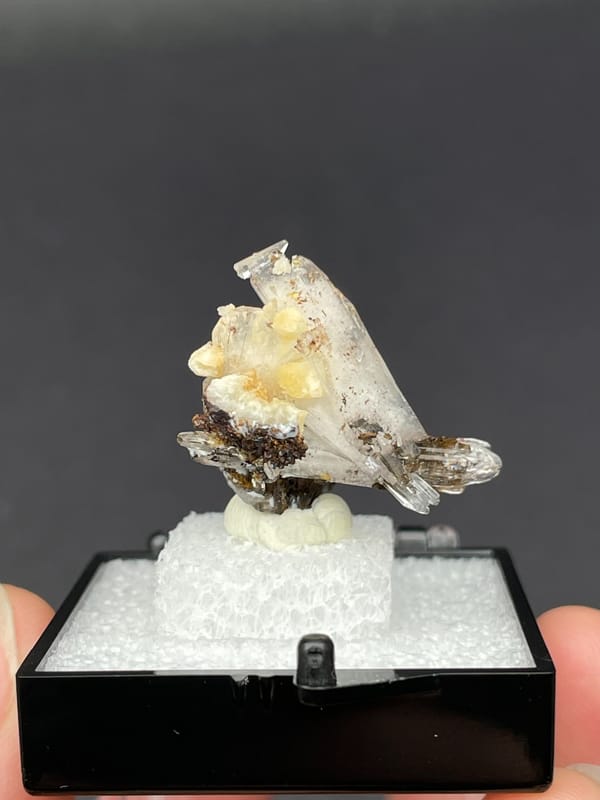 Colourless bladed creedite crystals with dark inclusions from Guizhou, China, detail of the matrix contact