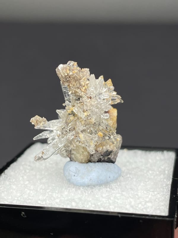 Colourless radiating creedite needle spray from Guizhou, China, in a display box, second angle