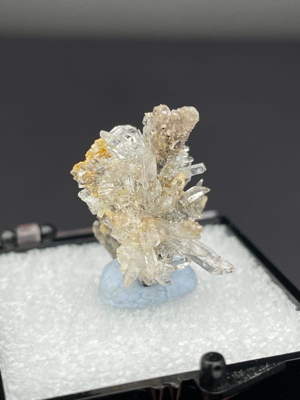 Colourless radiating creedite needle spray from Guizhou, China, in a display box, close-up of the crystal faces
