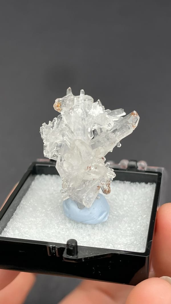 Colourless glassy creedite crystal spray from Guizhou, China, in a display box, detail of the matrix contact