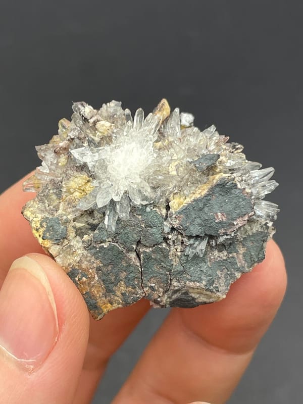 White creedite needle sprays on a grey-brown rock from Guizhou, China, close-up of the crystal faces