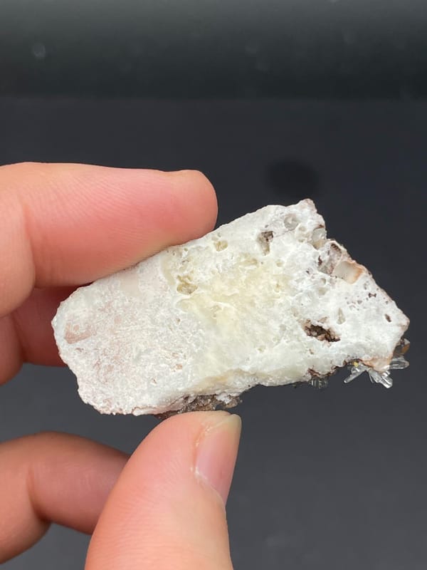 White creedite needle rosettes on brown rock from Guizhou, China, detail of the matrix contact