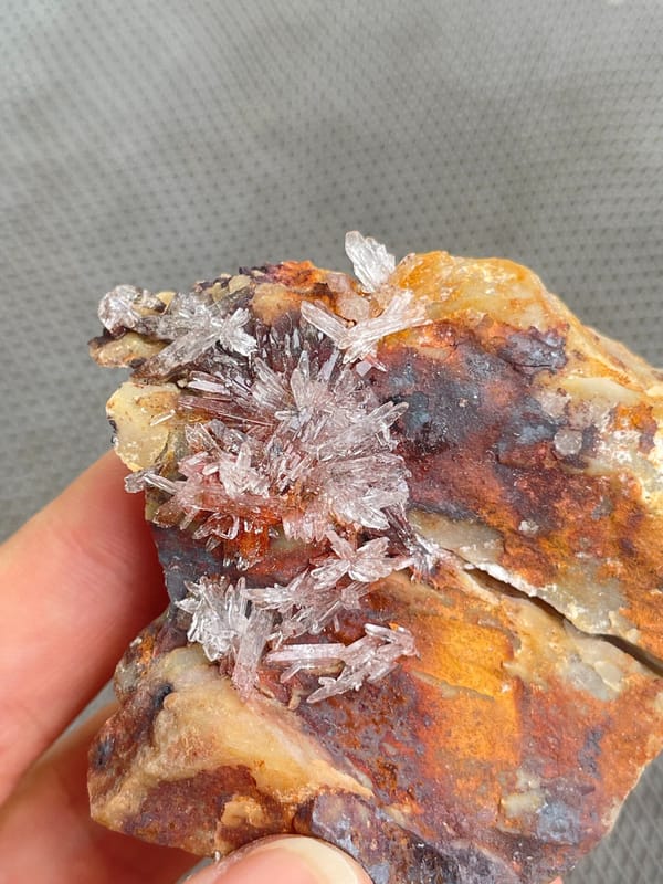 Pale creedite crystal crust on ochre-brown rock from Guizhou, China, close-up of the crystal faces