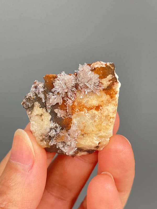 Pale creedite needle sprays on ochre-orange rock from Guizhou, China, close-up of the crystal faces