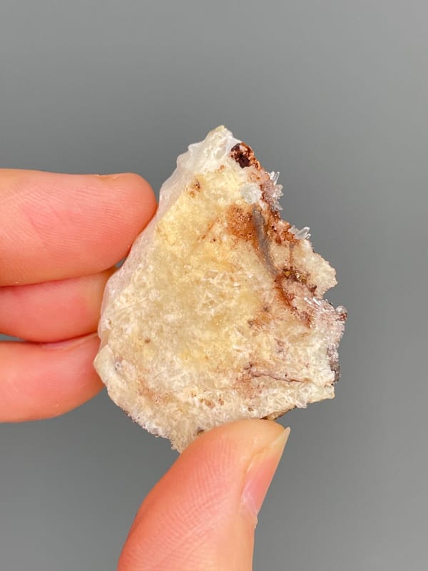 Pale creedite needle sprays on ochre-orange rock from Guizhou, China, detail of the matrix contact