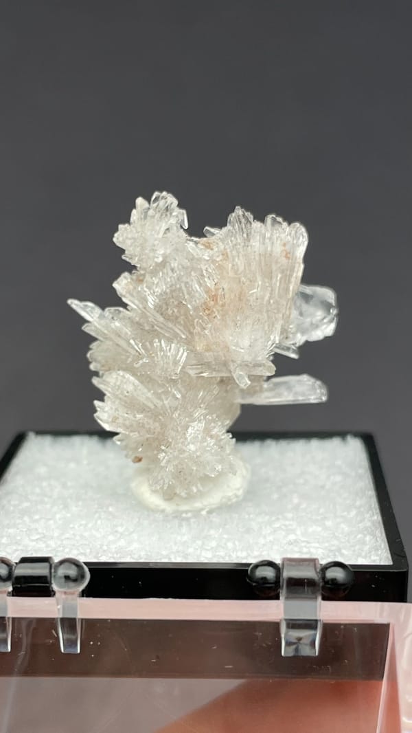 Colourless spiky radiating creedite spray from Guizhou, China, in a display box, close-up of the crystal faces