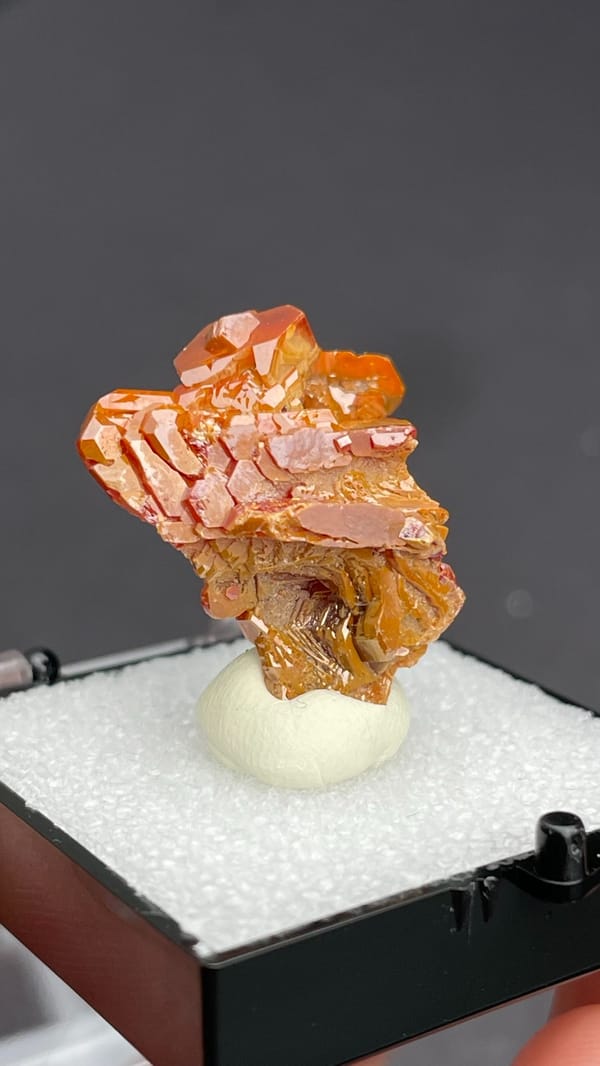 Layered orange-red vanadinite crystals from Morocco, in a display box, second angle
