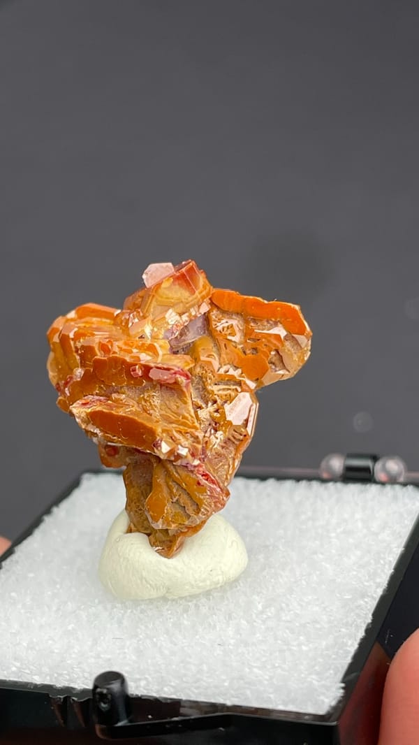 Layered orange-red vanadinite crystals from Morocco, in a display box, close-up of the crystal faces