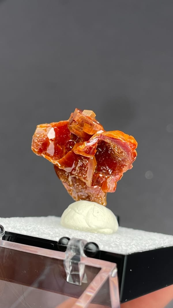 Layered orange-red vanadinite crystals from Morocco, in a display box, detail of the matrix contact