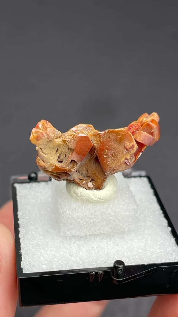 Orange vanadinite plates standing on a tan matrix from Morocco, in a box, second angle