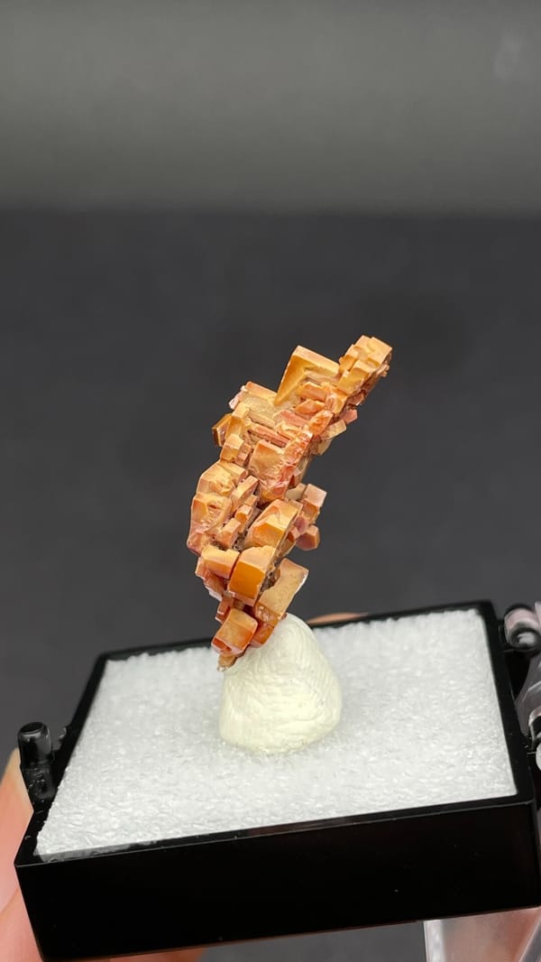 Stacked peach-red vanadinite crystal column from Morocco, in a display box, close-up of the crystal faces