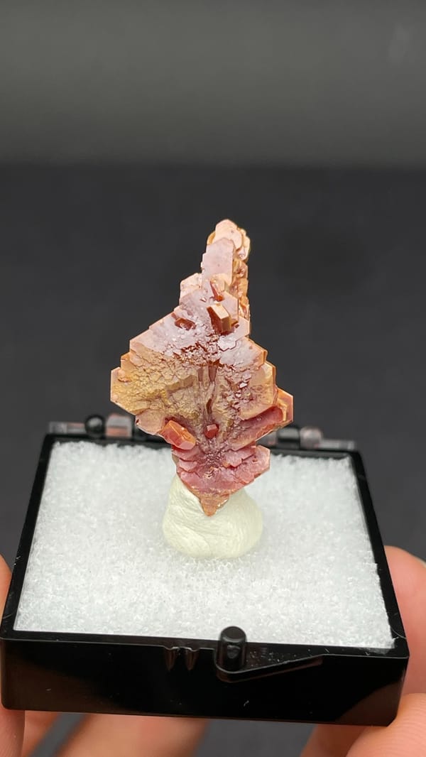 Stacked peach-red vanadinite crystal column from Morocco, in a display box, detail of the matrix contact