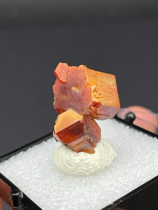 Stacked red-orange and amber vanadinite crystals from Morocco, in a box, second angle