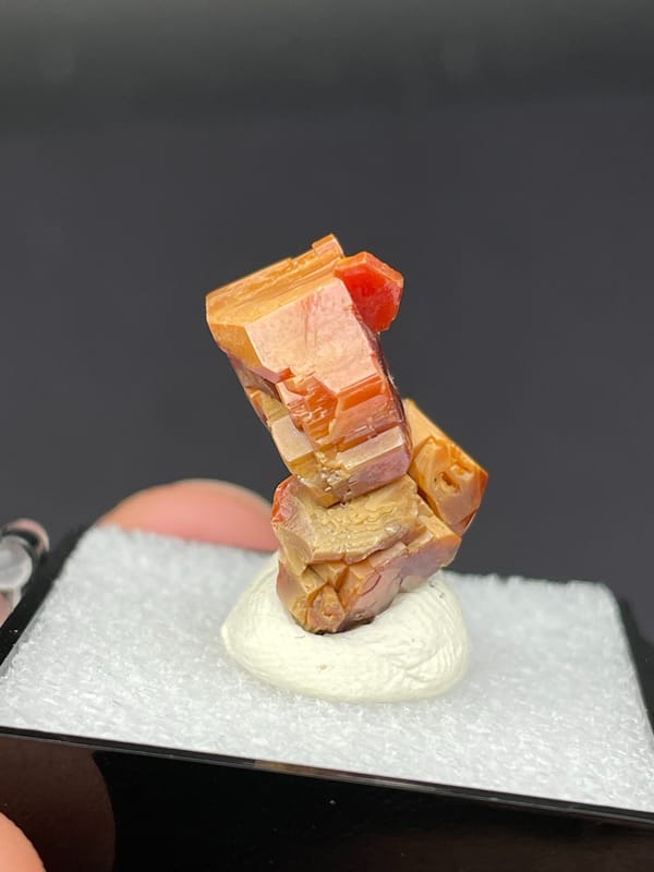 Stacked red-orange and amber vanadinite crystals from Morocco, in a box, reverse side