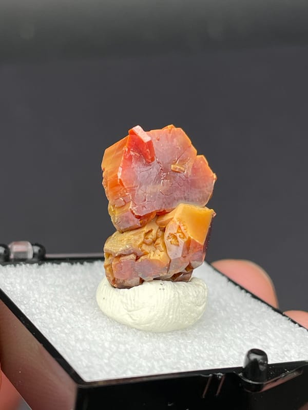 Stacked red-orange and amber vanadinite crystals from Morocco, in a box, detail of the matrix contact