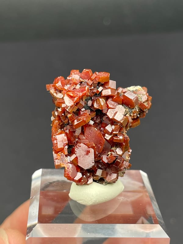 Matrix covered in red-orange vanadinite plates from Morocco, on an acrylic stand