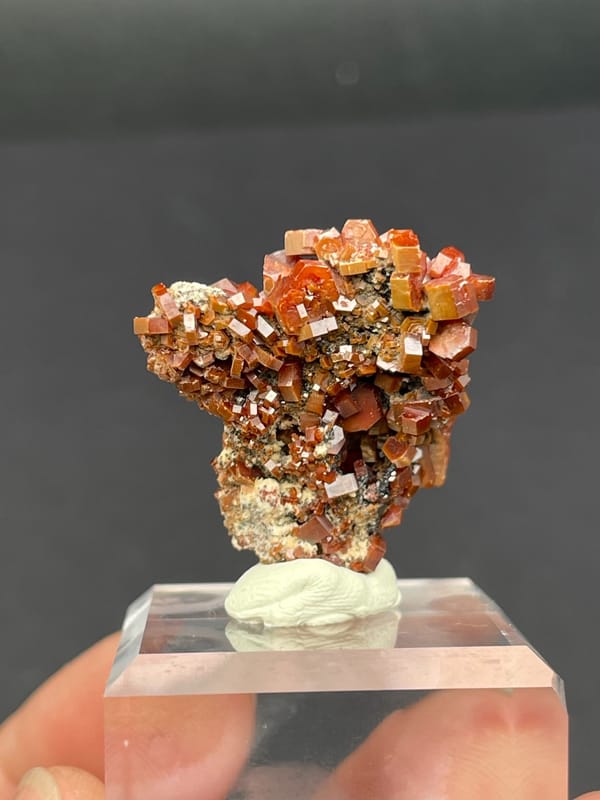 Matrix covered in red-orange vanadinite plates from Morocco, on an acrylic stand, second angle