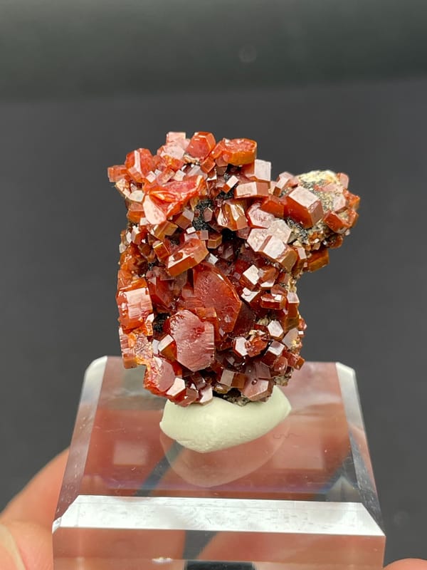 Matrix covered in red-orange vanadinite plates from Morocco, on an acrylic stand, reverse side