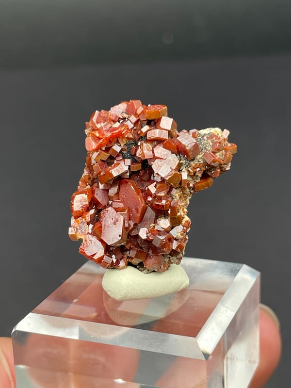 Matrix covered in red-orange vanadinite plates from Morocco, on an acrylic stand, top view