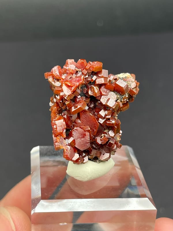 Matrix covered in red-orange vanadinite plates from Morocco, on an acrylic stand, detail of the matrix contact