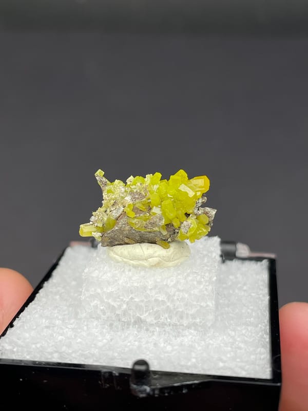 Yellow-green pyromorphite crust on grey matrix from Guangdong, China, in a box, close-up of the crystal faces
