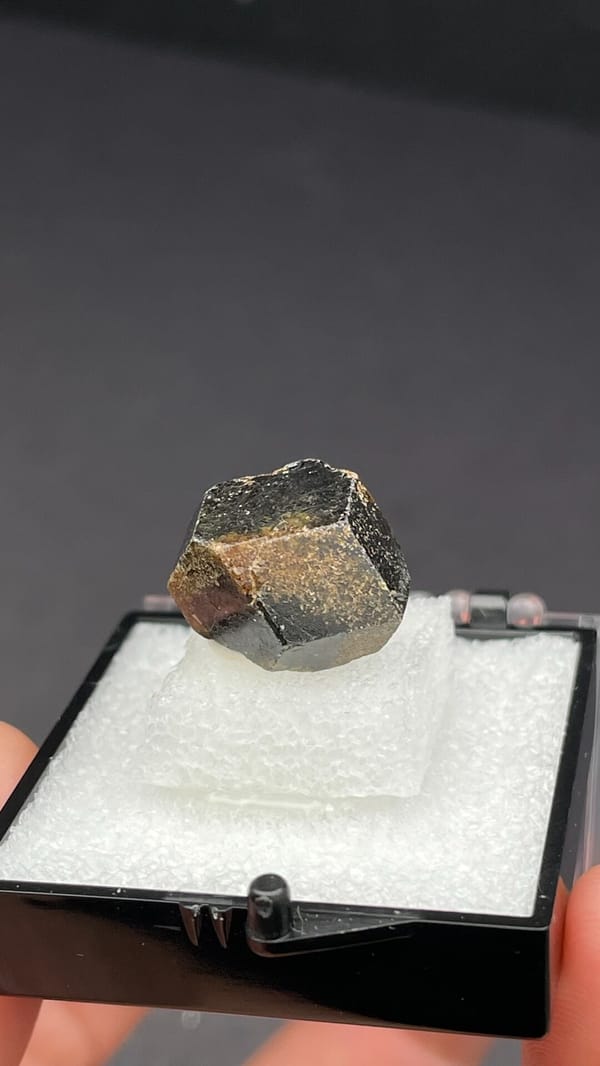 Brown dodecahedral andradite garnet crystal from Handan, Hebei, China, in a box, detail of the matrix contact