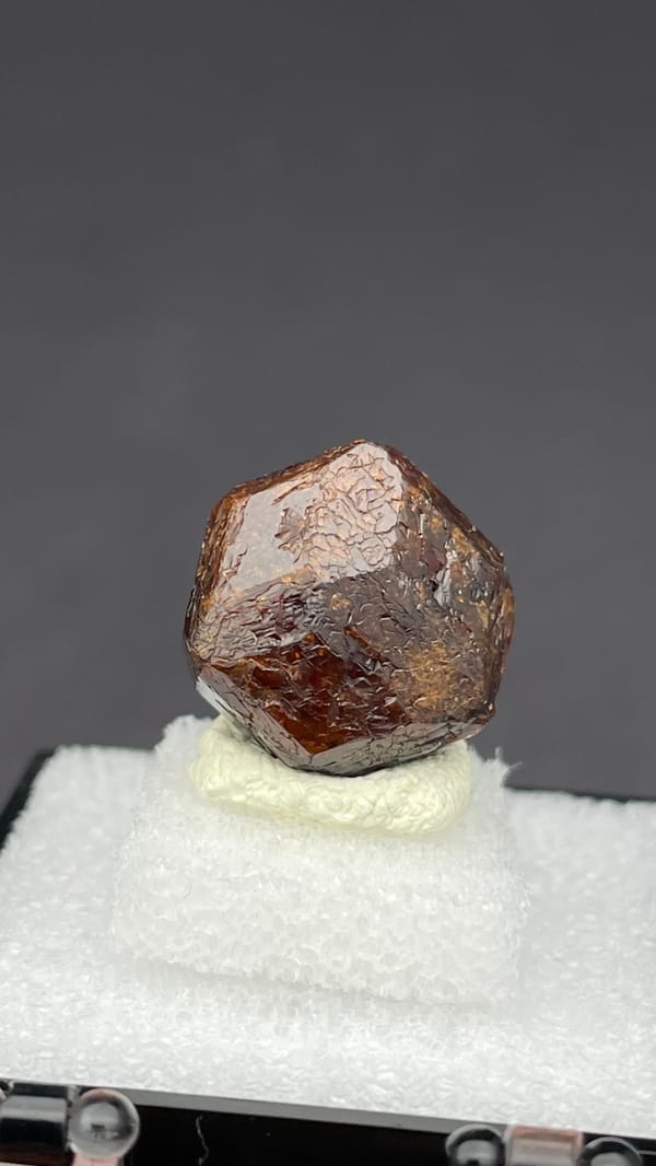 Dark red-brown dodecahedral andradite garnet from Handan, Hebei, China, in a box, close-up of the crystal faces