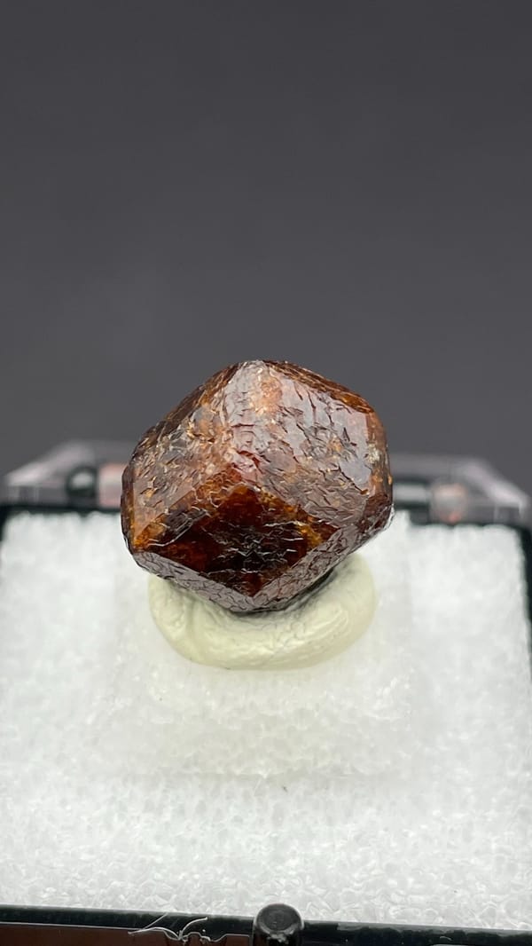 Dark red-brown dodecahedral andradite garnet from Handan, Hebei, China, in a box, detail of the matrix contact