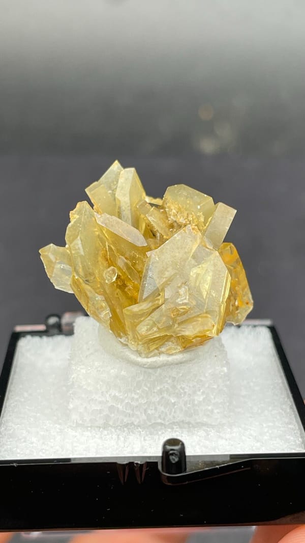 Golden-yellow baryte crystal cluster from Yunnan, China, in a display box, detail of the matrix contact