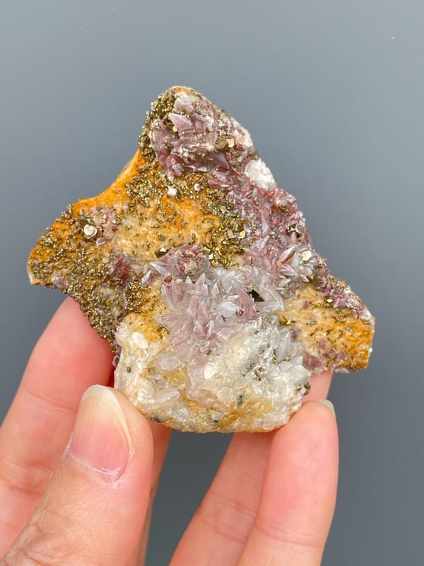 Golden pyrite crust over pale pink calcite from Hubei, China, held in hand