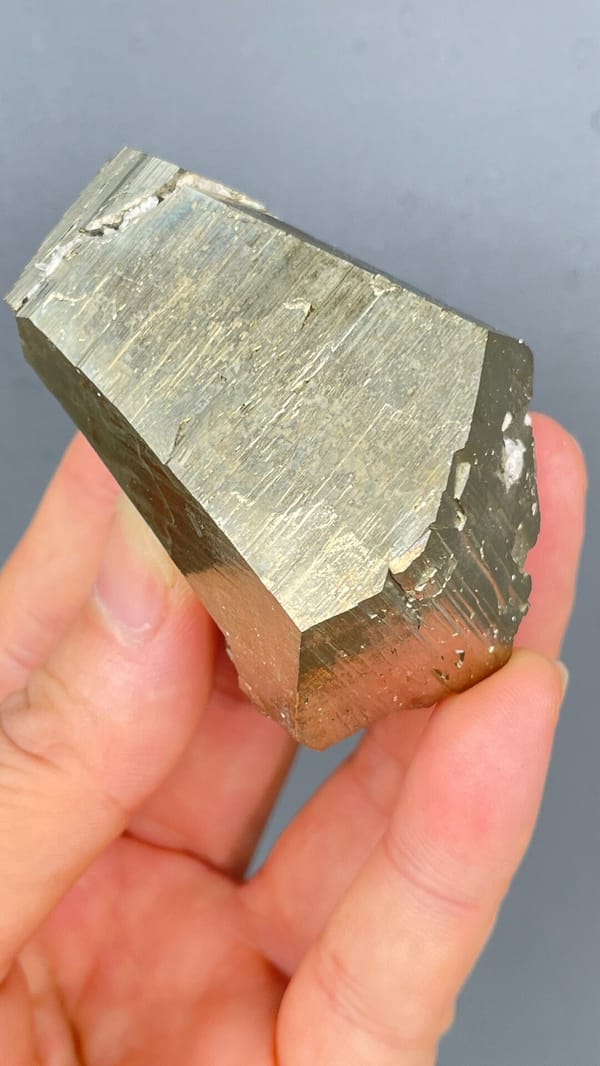 Large brassy striated pyrite single crystal from Yunnan, China, held in hand