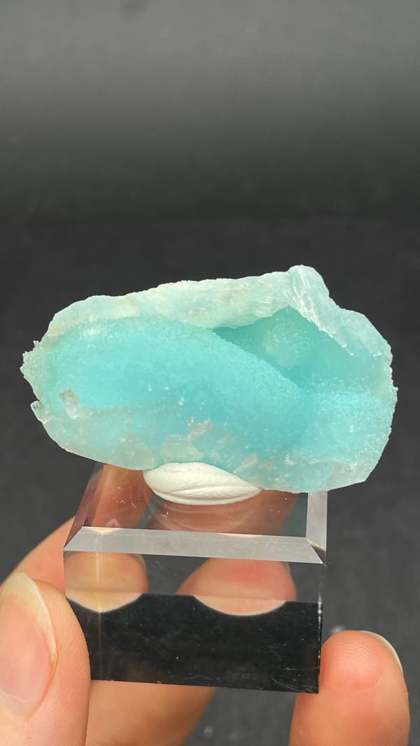 Turquoise-blue fibrous aragonite crust from Yunnan, China, on an acrylic stand, close-up of the crystal faces