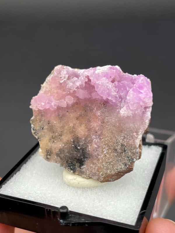 Magenta-pink botryoidal aragonite crust on pale slab from Yunnan, China, in a box, reverse side