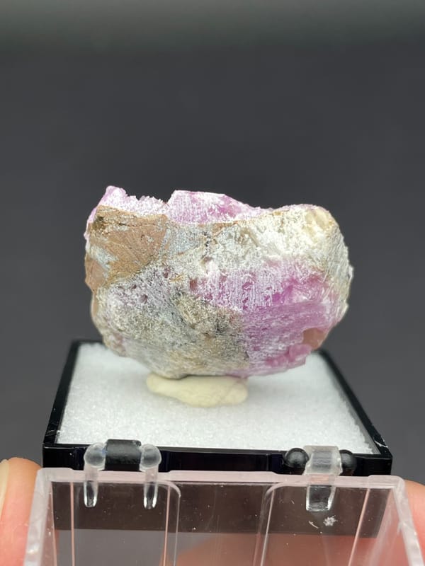 Magenta-pink botryoidal aragonite crust on pale slab from Yunnan, China, in a box, detail of the matrix contact
