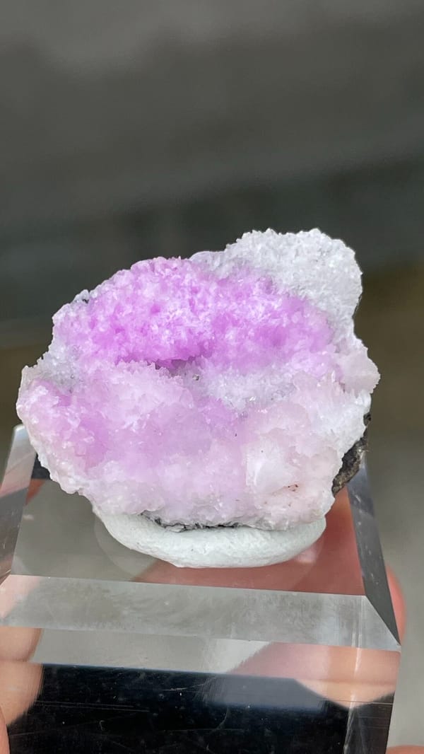 Magenta-pink aragonite cap on pale rock from Yunnan, China, on a stand