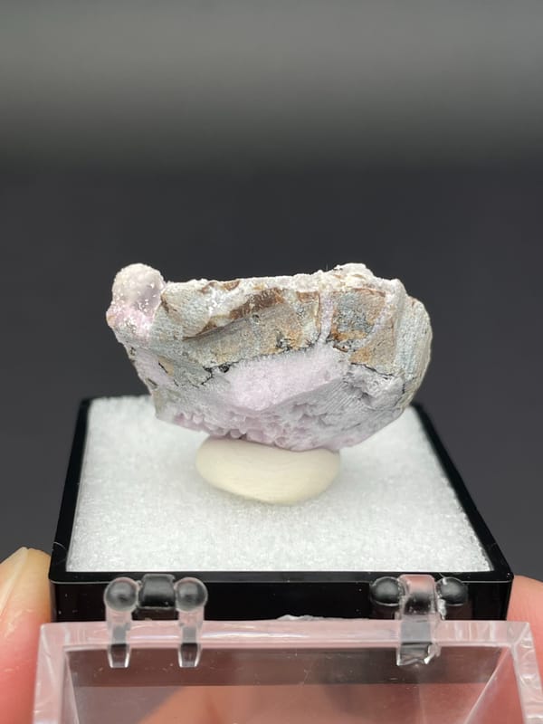 Pink-lilac botryoidal aragonite crust on pale slab from Yunnan, China, in a box, detail of the matrix contact