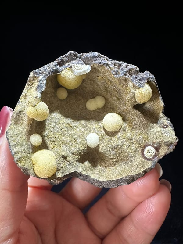 Cream calcite spheres inside a shallow rock cavity from Zhejiang China, specimen view 1