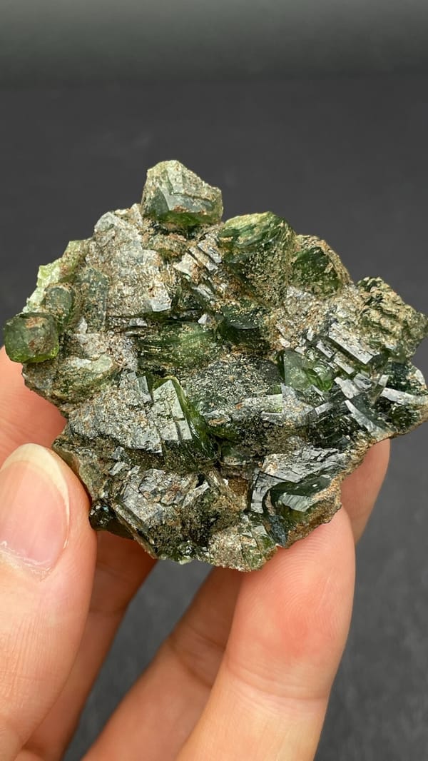 Apple-green ludlamite crystals on grey matrix from Brazil, held in hand
