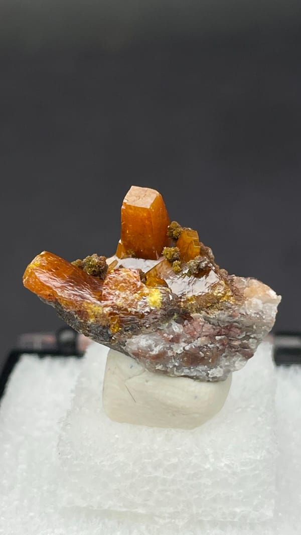 Bright orange wulfenite crystals on brown matrix from Mexico, in a display box, detail of the matrix contact