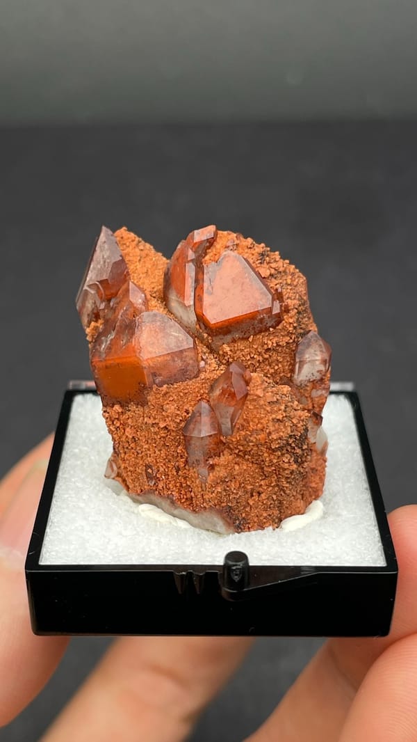 Red hematoid quartz with black specular hematite from Shanxi, China, in a perky box, detail of the matrix contact