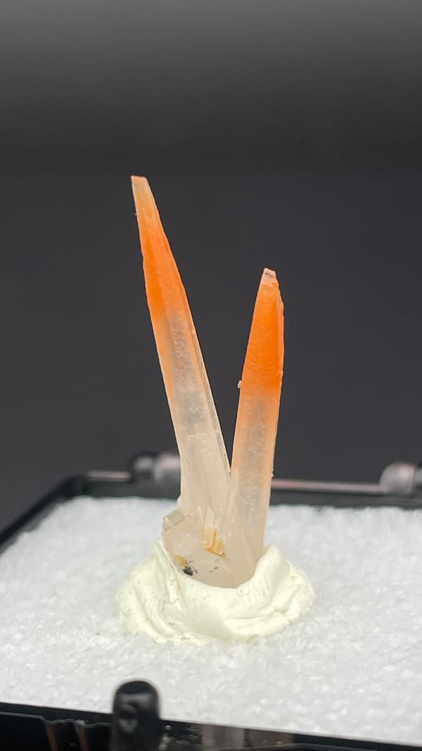 Two slender orange-red hematoid quartz needles from Guangdong, China, in a perky box, top view
