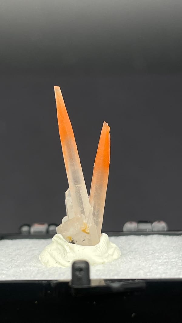 Two slender orange-red hematoid quartz needles from Guangdong, China, in a perky box, detail of the matrix contact
