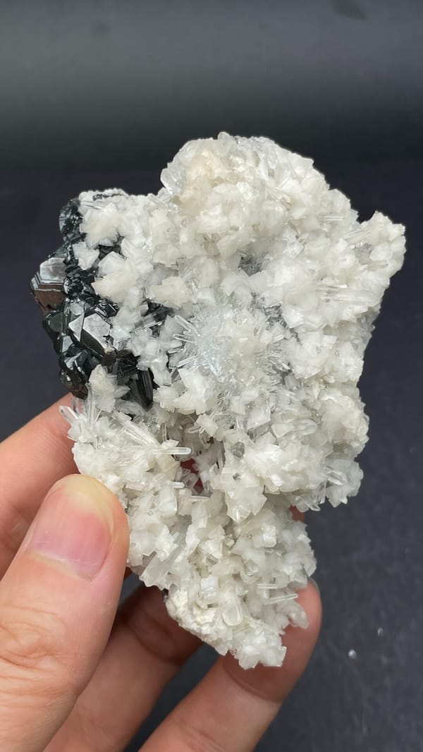 White quartz crust over dark marmatite sphalerite from Peru, held in hand