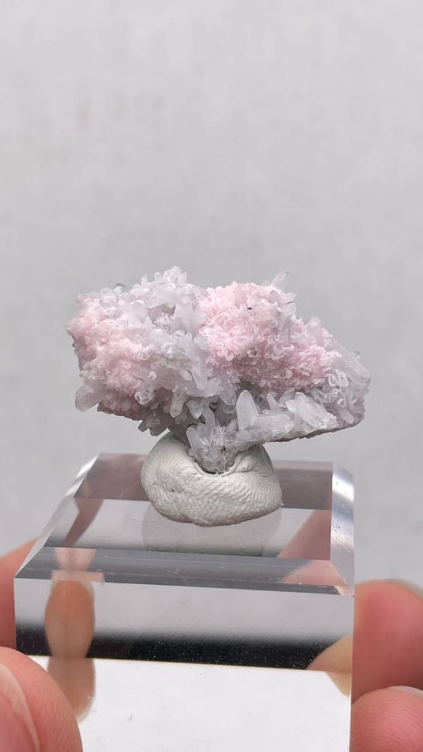 Pale pink rhodochrosite crust on quartz from Romania, on an acrylic stand