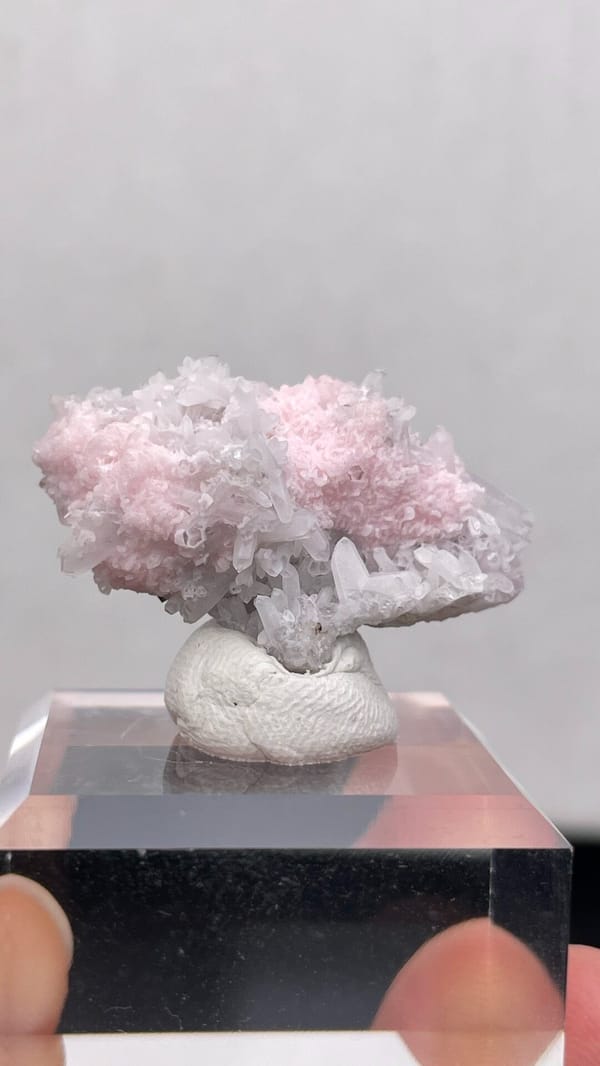 Pale pink rhodochrosite crust on quartz from Romania, on an acrylic stand, close-up of the crystal faces