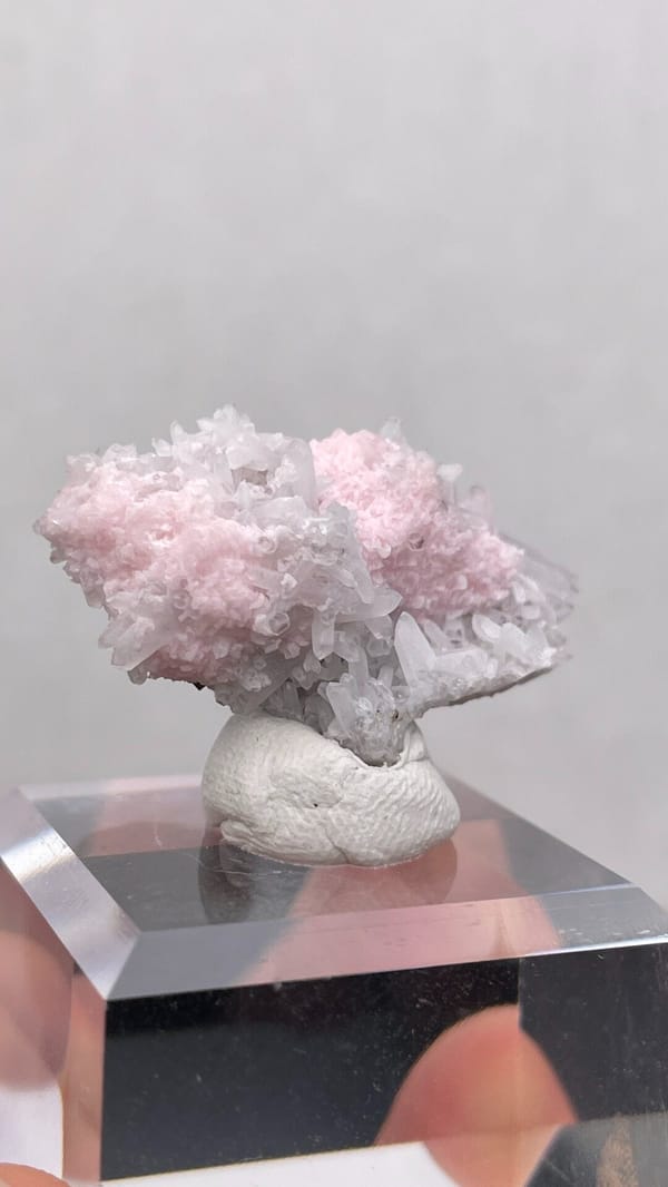 Pale pink rhodochrosite crust on quartz from Romania, on an acrylic stand, reverse side