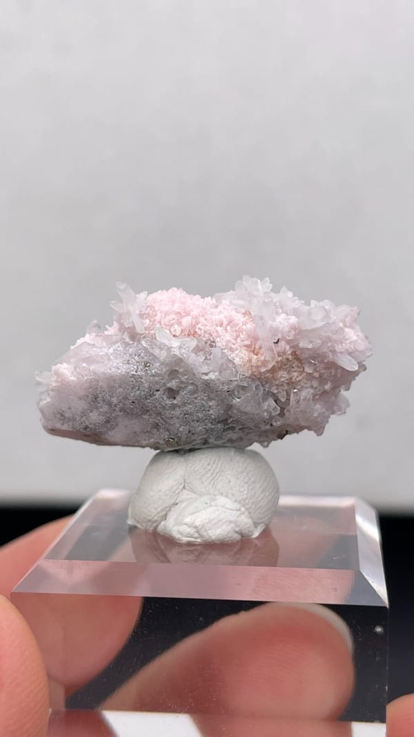 Pale pink rhodochrosite crust on quartz from Romania, on an acrylic stand, detail of the matrix contact