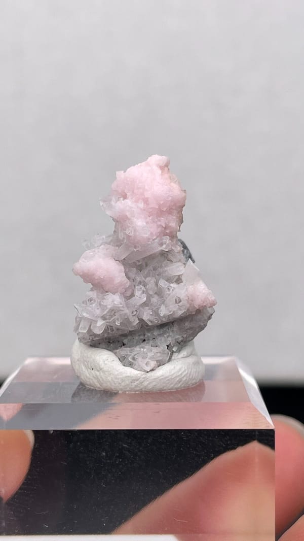 Pale pink rhodochrosite crust on grey quartz from Romania, on an acrylic stand
